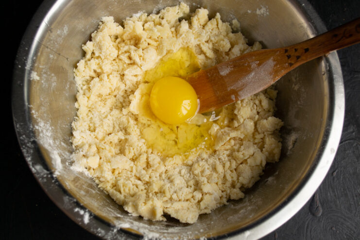 An egg being added to the flour and butter crumb mixture in a bowl.