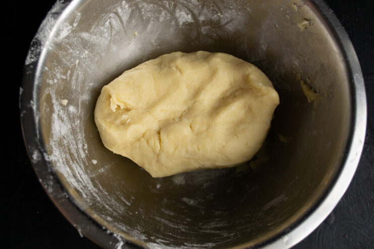 A ball of shortcrust pastry dough wrapped in plastic wrap, ready for chilling in the refrigerator.