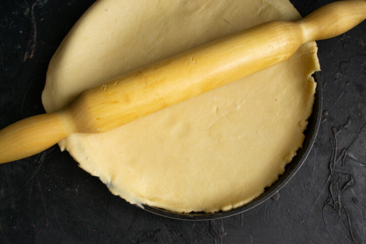Chilled pie dough being rolled out with a rolling pin on a floured surface.