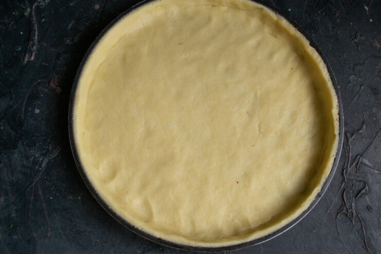 Trimming the excess dough from the edges of a tart pan to create a neat crust.