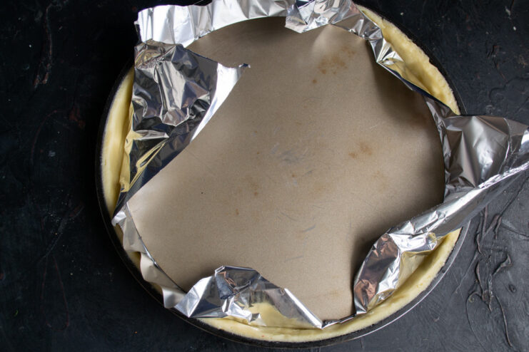 Pressing down the center of the dough in a tart pan, covered with foil and pie weights.