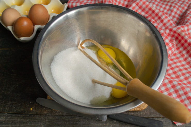 Step 2: Adding Sugar and a Pinch of Salt to the Eggs Granulated sugar and salt being added to the eggs in the mixing bowl.