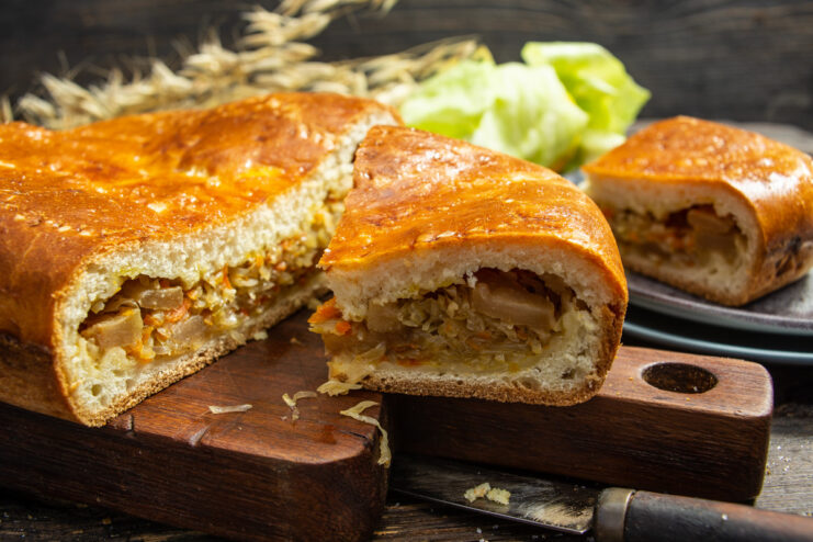 A whole baked golden-brown cabbage pie on a wooden surface.