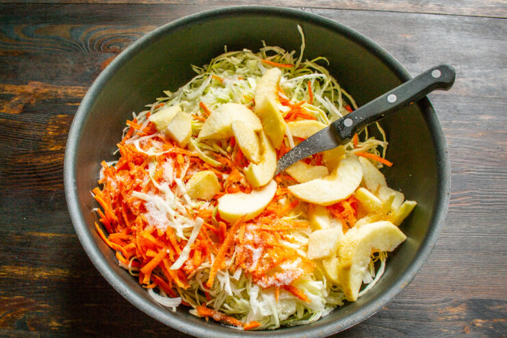 Adding Apple to the Cabbage Filling for Sweetness Sliced apples being added to a pan with sautéed cabbage and carrots.