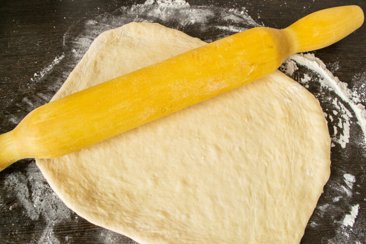 Rolling Out the Yeast Dough for the Cabbage Pie A piece of dough being rolled out into a rectangle on a floured surface.