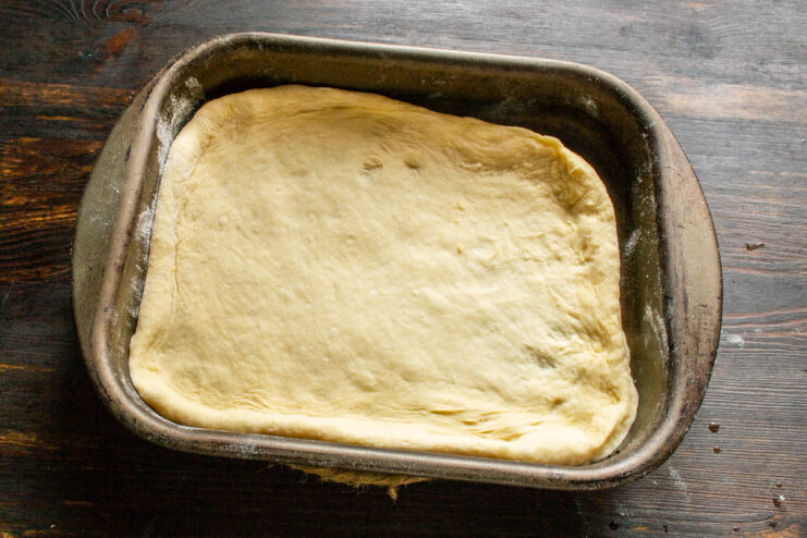 Lining the Baking Dish with the Bottom Layer of Dough The bottom layer of dough pressed into a rectangular baking dish.