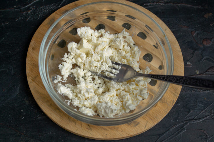 Crumbling Brynza Cheese for the Filling A bowl of crumbled brynza cheese being mashed with a fork for the pirozhki filling.