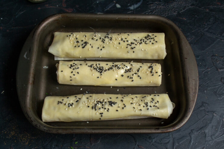 Sprinkling with Sesame Seeds Before Baking Close-up of pirozhki being sprinkled with black and white sesame seeds before going into the oven.