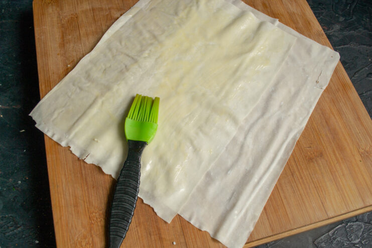 Preparing the Phyllo Dough Sheets A sheet of phyllo dough being cut in half with a knife on a cutting board.