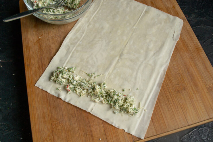 Adding the Savory Filling to the Phyllo Dough A thin line of cheese and herb filling being placed on the edge of a buttered phyllo dough strip.
