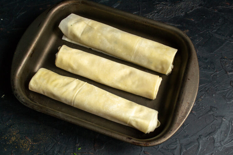Arranging the Pirozhki on a Baking Sheet Unbaked phyllo dough pirozhki arranged in neat rows on a baking sheet lined with parchment paper.