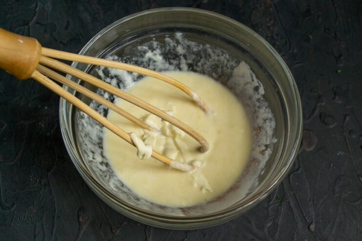 Whisking Mayonnaise into the Pirozhki Batter Whisking mayonnaise into the egg and smetana mixture in a glass bowl.