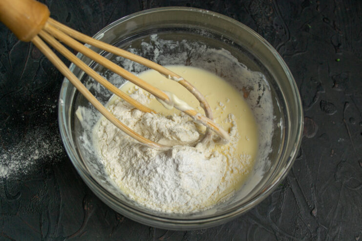 Adding Dry Ingredients to the Batter Adding flour and baking powder to the wet ingredients for the pirozhki batter.