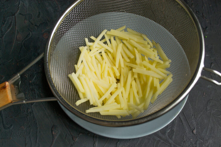 Preparing the Potato Base for Pirozhki Julienned potatoes being rinsed with cold water in a colander.