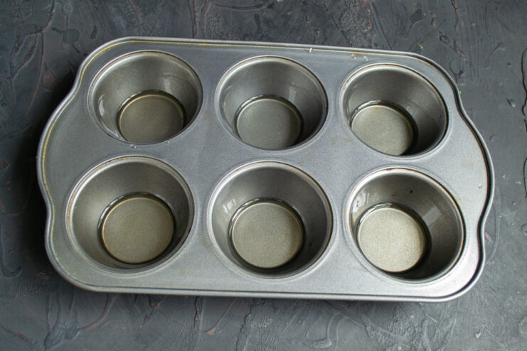 Preheating Oil in the Muffin Tin A muffin tin with oil in each cup being placed in the oven to preheat.
