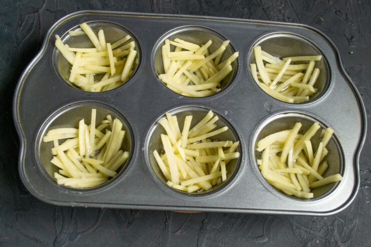 Creating the Crispy Potato Layer Placing a layer of julienned potatoes into the hot oil in each cup of the muffin tin.