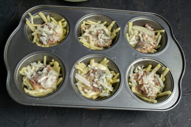 Adding the Saury and Onion Filling Placing pieces of canned saury and chopped onion on top of the batter layer in the muffin tin.
