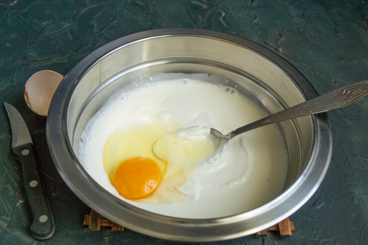 Mixing Wet Ingredients for Pirozhki Dough A glass bowl containing kefir, smetana, and a cracked egg, ready for mixing.