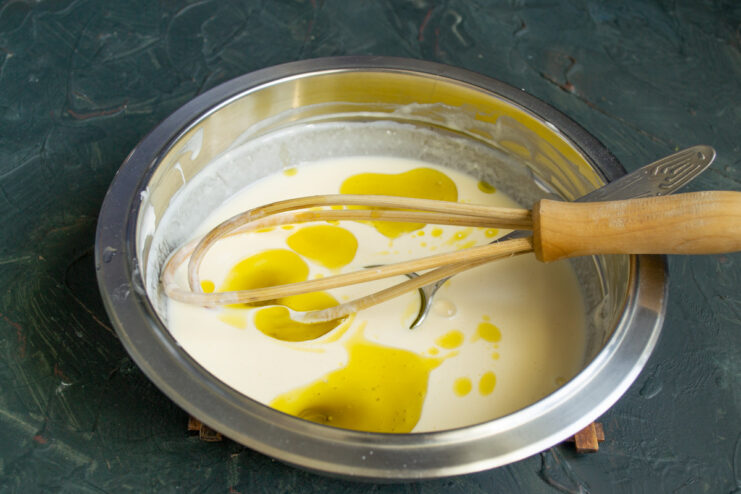 Whisking the Kefir and Egg Mixture A hand using a whisk to combine egg, smetana, and kefir in a glass bowl.
