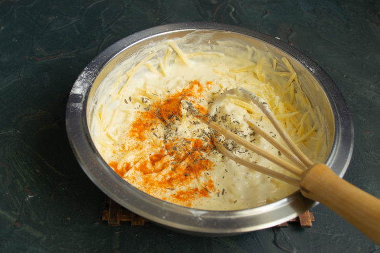Seasoning the Cheese Batter Sprinkling ground paprika and dried thyme into the cheese batter in a bowl.