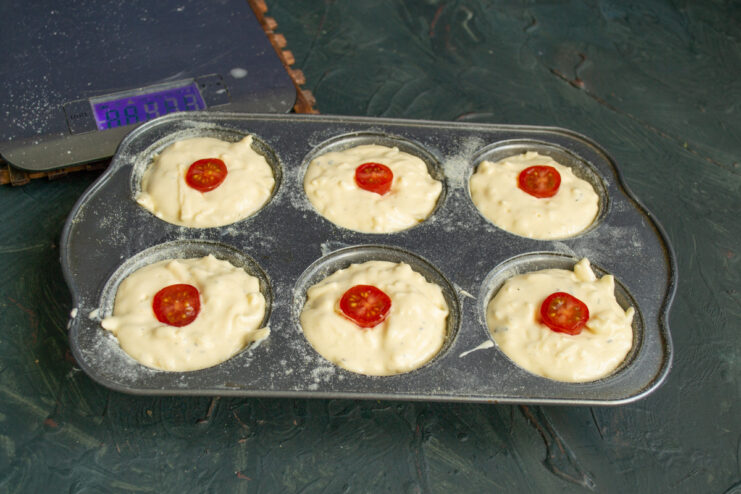Topping Pirozhki with Cherry Tomatoes Placing halved cherry tomatoes on top of the batter in each cup of a muffin tin.