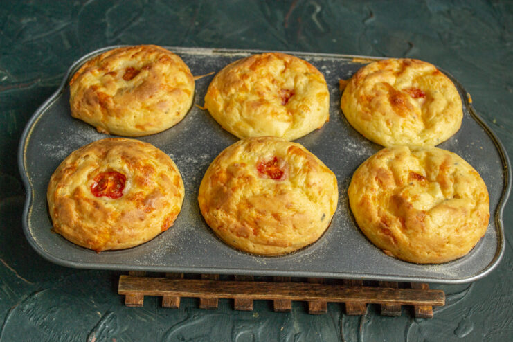 Freshly Baked Golden-Brown Cheese Pirozhki A batch of freshly baked, golden-brown kefir cheese pirozhki in a muffin tin.