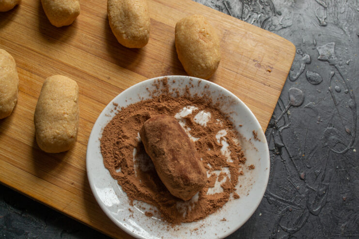 Coating the chocolate potato cakes in cocoa powder A shaped chocolate potato cake being rolled in a saucer of unsweetened cocoa powder.