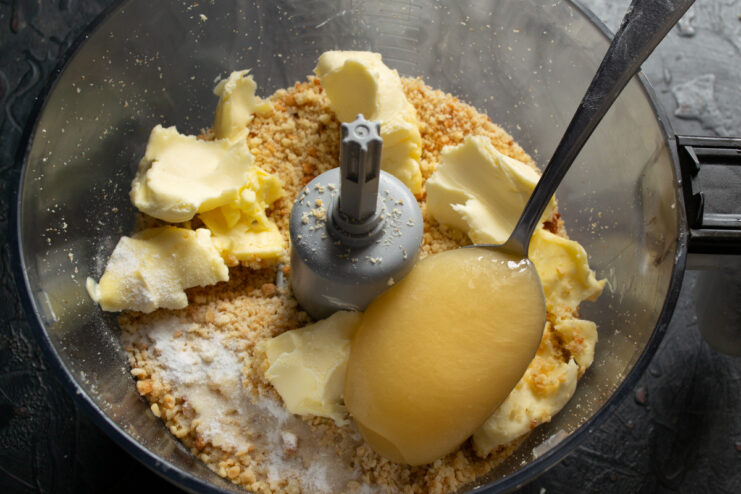 Adding softened butter to the mixture Adding a block of softened butter to the mixture of cake crumbs and nuts.