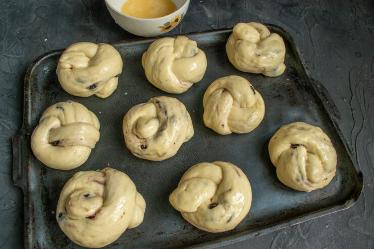 Step 12: Brushing the risen buns with egg wash for a golden finish. A pastry brush applying a thin layer of egg wash to the risen plyushki before baking.
