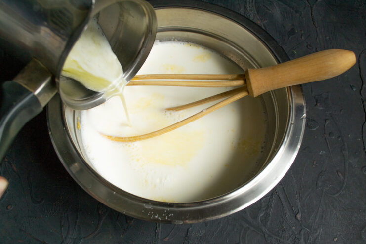 Step 3: Adding melted butter to the wet ingredients. Pouring melted butter from a small saucepan into the bowl with the milk and egg mixture.
