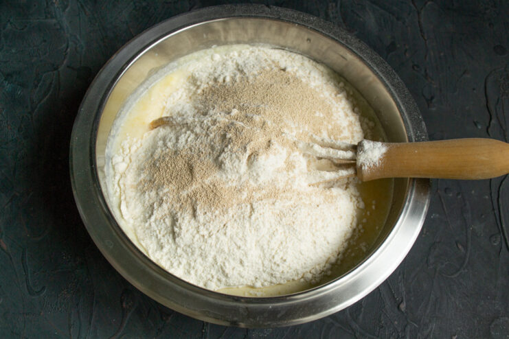Step 5: Adding instant yeast on top of the flour. Sprinkling a spoonful of instant yeast over the mound of sifted flour in the mixing bowl.
