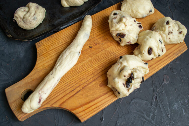 Step 9: Rolling a piece of dough into a long rope. Hands rolling a portion of dough into a long, thin rope shape on a wooden board.