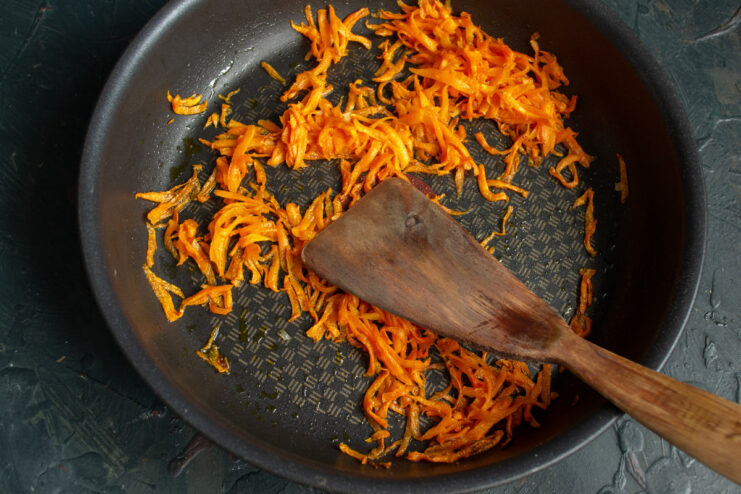Sautéing Grated Carrots for Flavor Grated carrots being sautéed in a frying pan until tender.