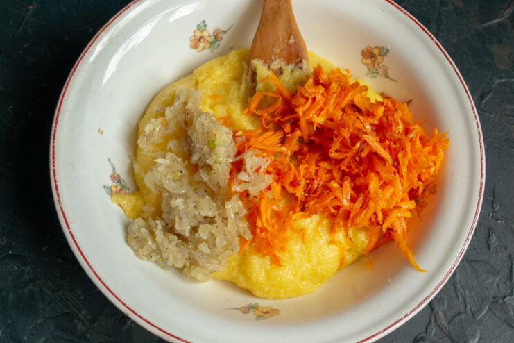 Combining Sautéed Vegetables with Hot Polenta Mixing sautéed carrots and onions into the pot of hot, cooked polenta.