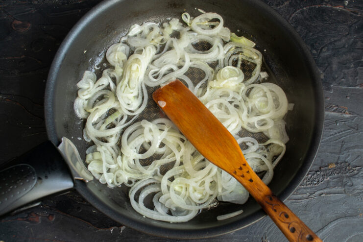 Preparing the onions for frying until golden brown. A yellow onion being sliced into thin rings on a wooden cutting board.