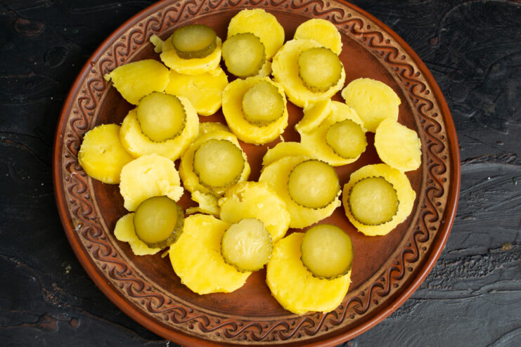 Layering the base of the salad with potatoes and pickles. A platter with alternating layers of sliced boiled potatoes and pickled cucumbers.