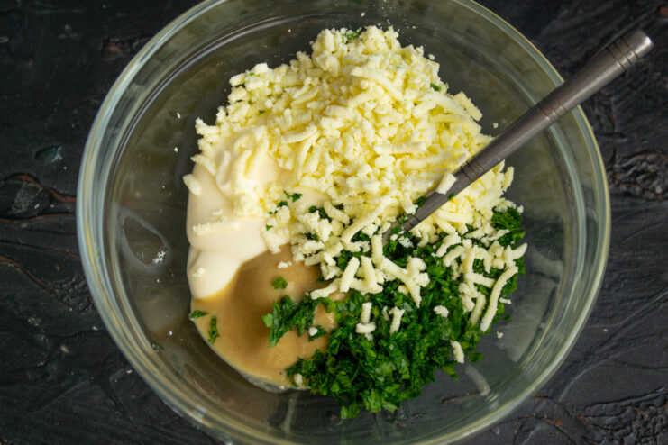 Mixing the creamy dressing with mayonnaise, mustard, and egg yolks. A bowl with ingredients for the salad dressing: mayonnaise, grated egg yolks, and herbs.