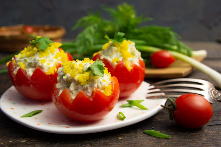 A plate of three tomatoes stuffed with a creamy cottage cheese and herb filling, garnished with parsley.