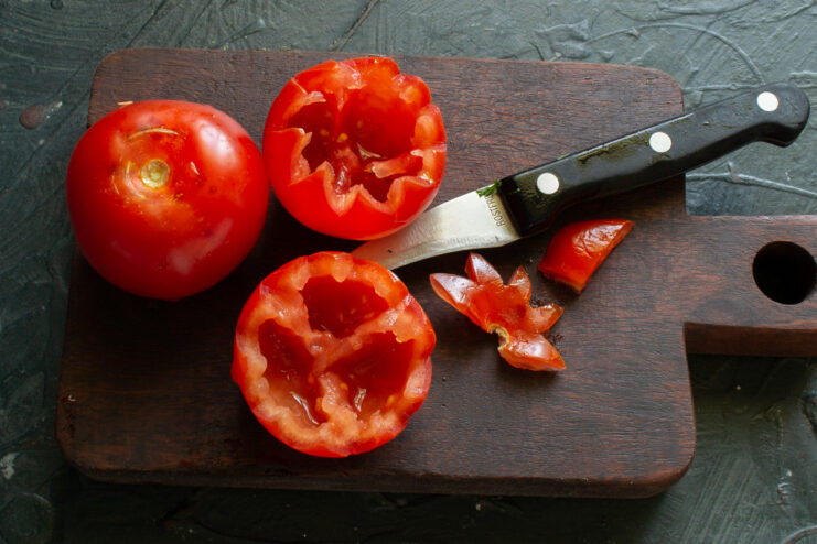 A person's hands using a small knife to carve out the inside of a tomato to prepare it for stuffing.