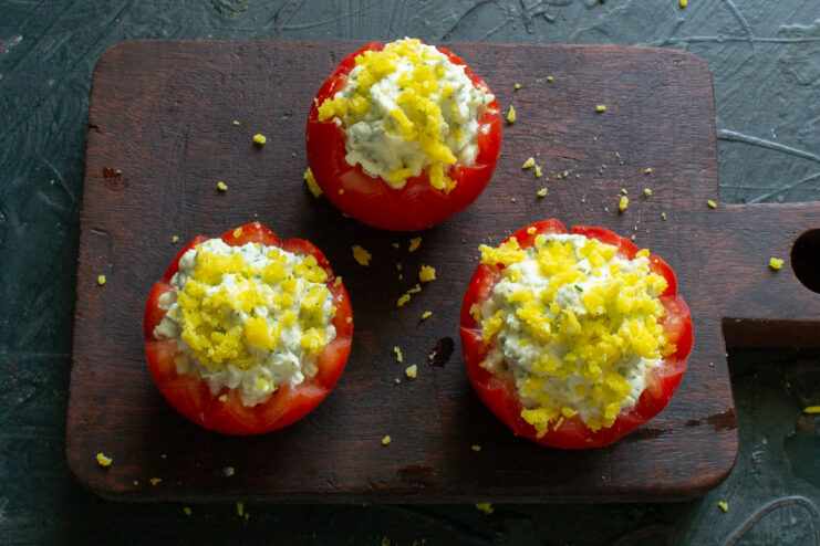 Crumbled egg yolk being sprinkled over the stuffed tomatoes for a colorful garnish.