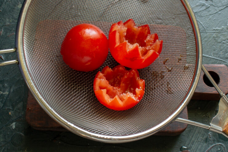 Hollowed-out tomatoes placed upside down in a white colander to drain before being stuffed.