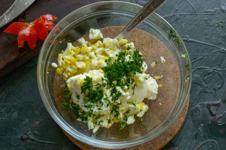 Finely chopped fresh dill being added to the cottage cheese and egg mixture in a bowl.