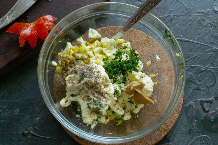 Mustard and mayonnaise being added to the filling mixture in a bowl to enhance flavor.