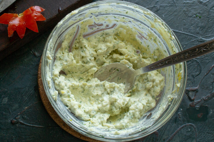 A spoon mixing the cottage cheese, egg, herbs, and mayonnaise in a bowl until well combined.