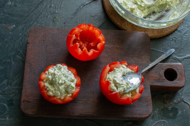A hand using a spoon to stuff a hollowed-out tomato with the creamy cottage cheese filling.
