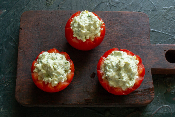 A close-up of a stuffed tomato with a generous mound of creamy filling on top.
