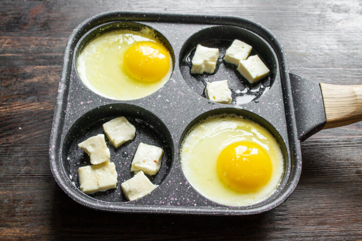 Pan-Frying Cubed Curd Cheese Cubed curd cheese being fried in the empty sections of the pan next to the eggs.