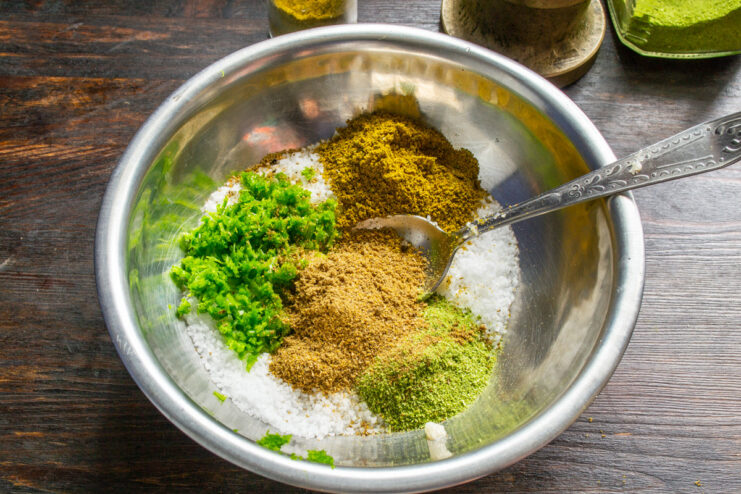 Combining the Freshly Ground Spices with the Salt Base Freshly ground spices being poured from a grinder into the bowl with salt and garlic.