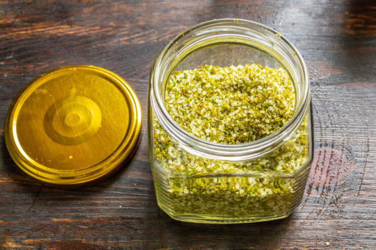 Storing the Finished Garlic Scape Salt for Long-Lasting Flavor The finished green spiced salt being transferred into a clean, dry glass jar for storage.