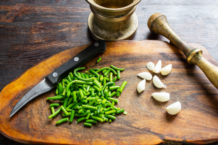 Chopping Garlic Scapes into Small Pieces Close-up of finely chopped green garlic scapes on a wooden cutting board.